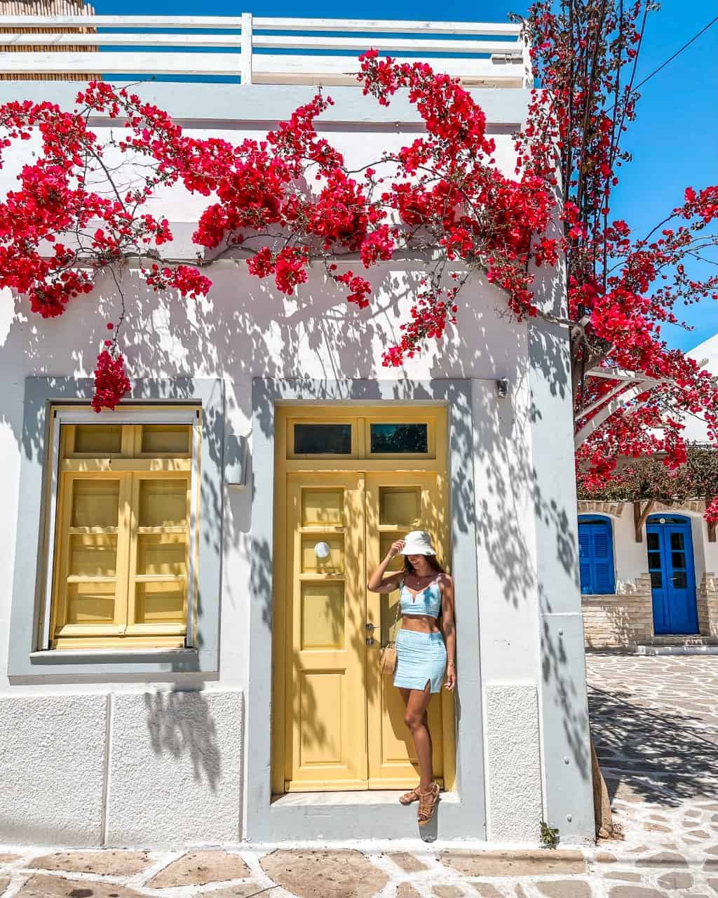 A photo of me posing in front of a yellow door next to a yellow window of a building framed by vibrant bougainvillea flowers.