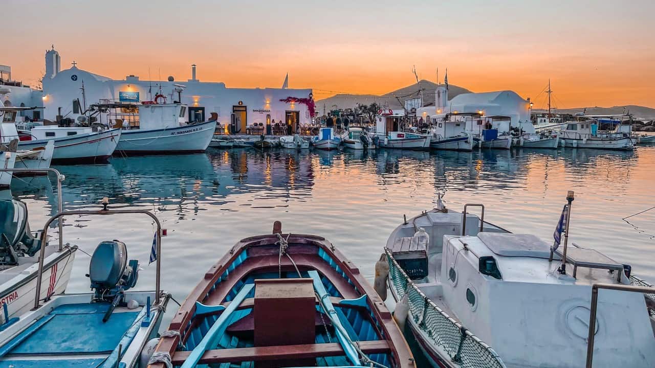 Sunset at the waterfront of Naoussa, Paros, with fishing boats anchoring in the harbor amidst charming tavernas.
