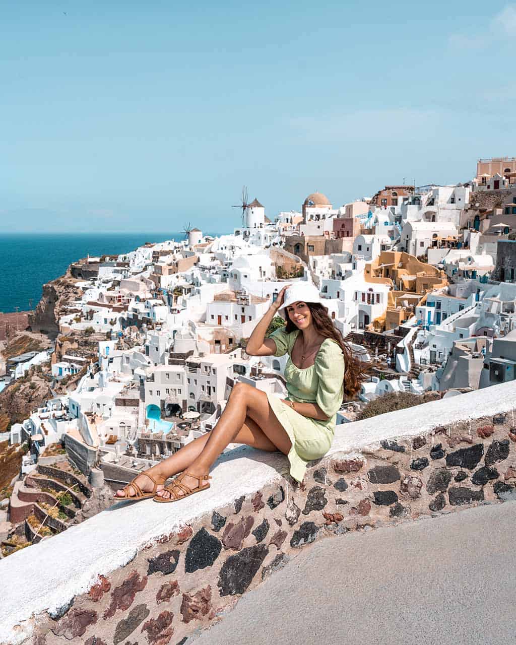 A photo of me sitting at the viewpoint of Oia Castle, surrounded by white-washed buildings, a charming windmill, and the sea in the background.