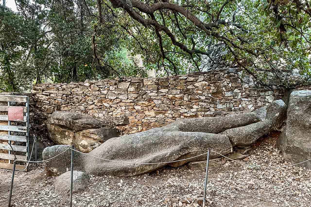Broken Kouros statue lying under trees