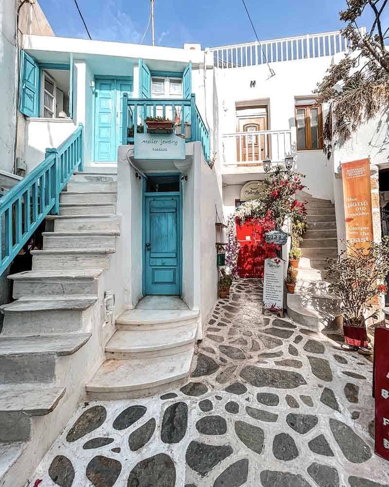 A charming corner of Naxos Town, featuring traditional white Cycladic buildings, blue doors, and cobblestone streets.