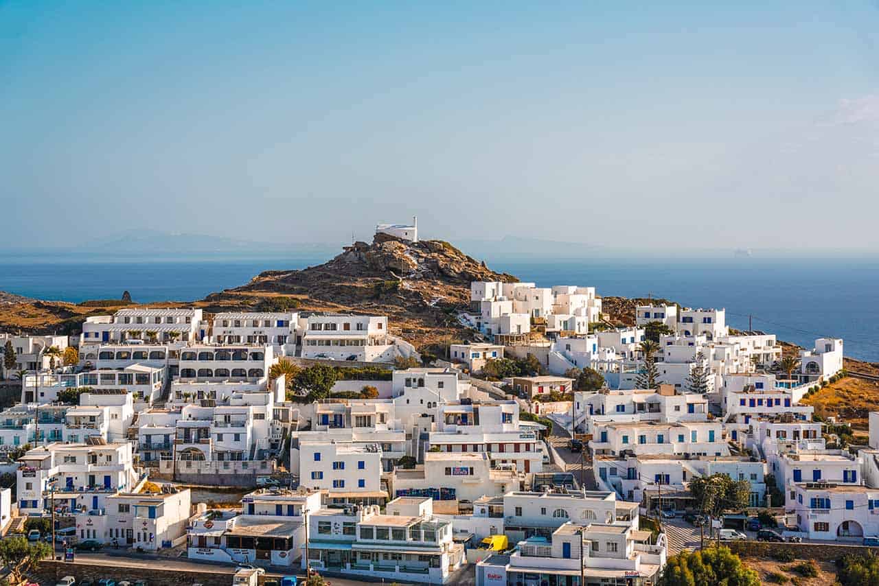 A charming Greek village in the Cyclades, characterized by its traditional white houses adorned with blue windows, set against the backdrop of the shimmering azure Aegean Sea.