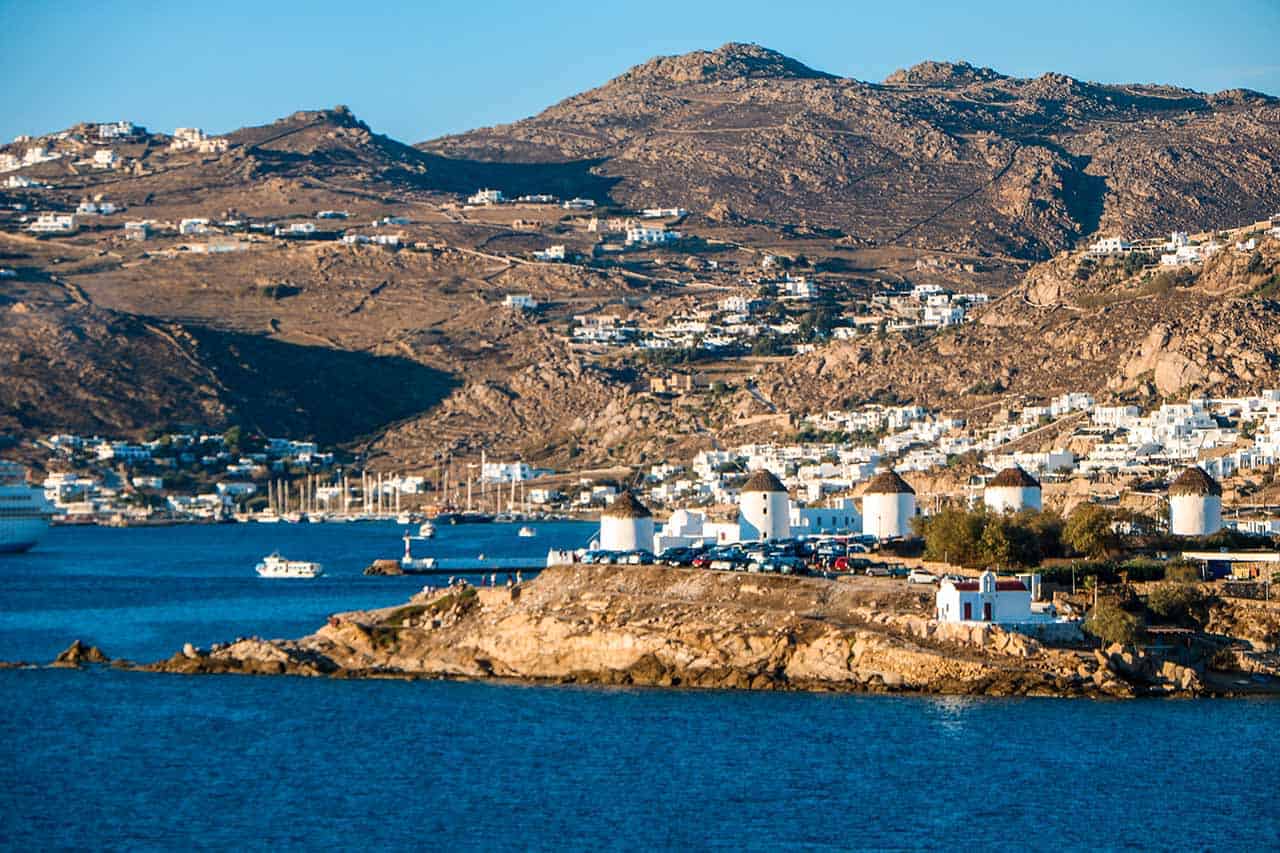 The iconic windmills of Mykonos stand proudly against the backdrop of the vibrant blue sea and rugged, rocky hills.