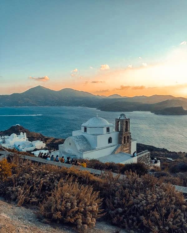 Dreamy view of a white church set against the backdrop of the shimmering sea and a breathtaking sunset.