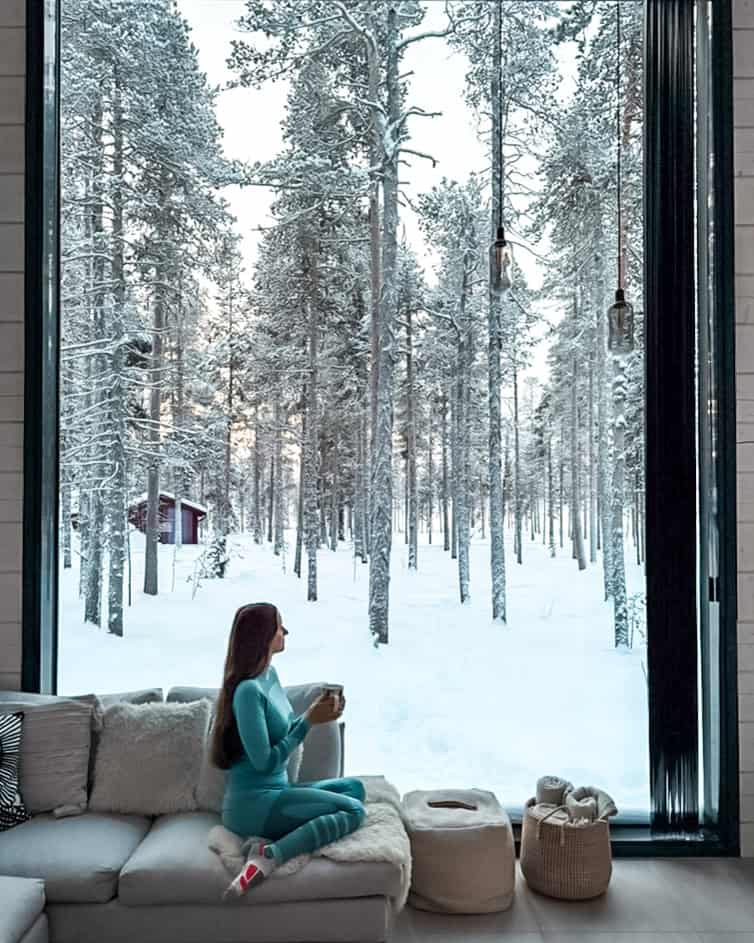 Me wearing my thermal base layers sitting in front of a large glass window and holding a cup of coffee while admiring the snowy landscape outside