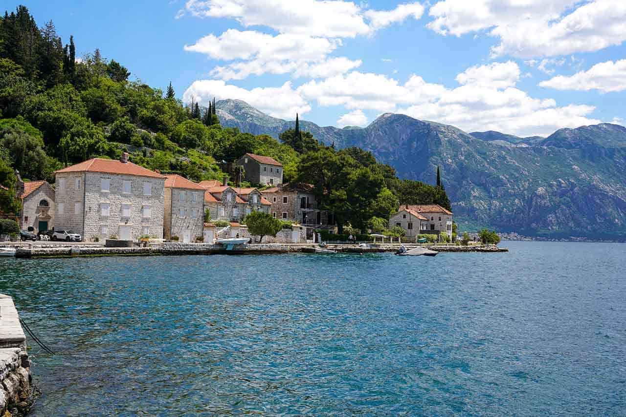 Montenegro's picturesque waterfront at Kotor Bay: Old stone houses with red rooftops and impressive mountains in the background.